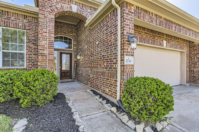 entrance to property with a garage, brick siding, and driveway