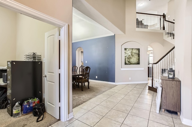 entryway featuring baseboards, light tile patterned flooring, arched walkways, stairs, and light carpet