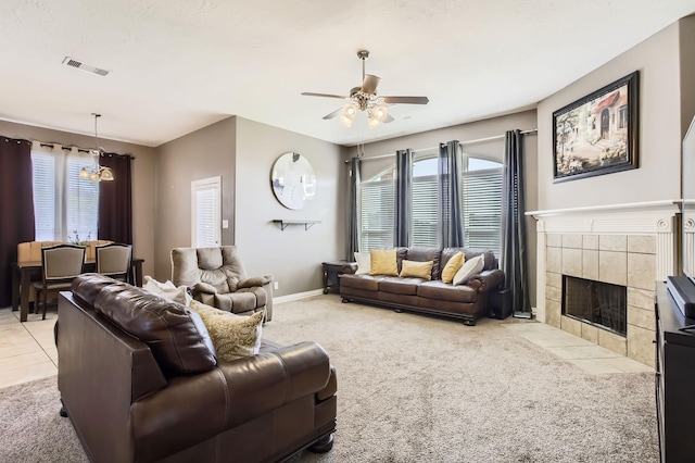 living room with visible vents, baseboards, ceiling fan, a tiled fireplace, and light colored carpet