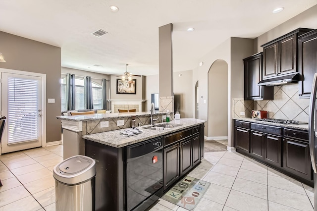 kitchen featuring light tile patterned floors, arched walkways, a sink, black dishwasher, and under cabinet range hood