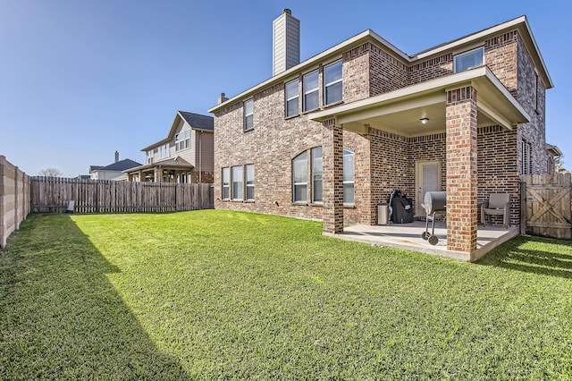 back of house with brick siding, a chimney, a fenced backyard, a yard, and a patio area