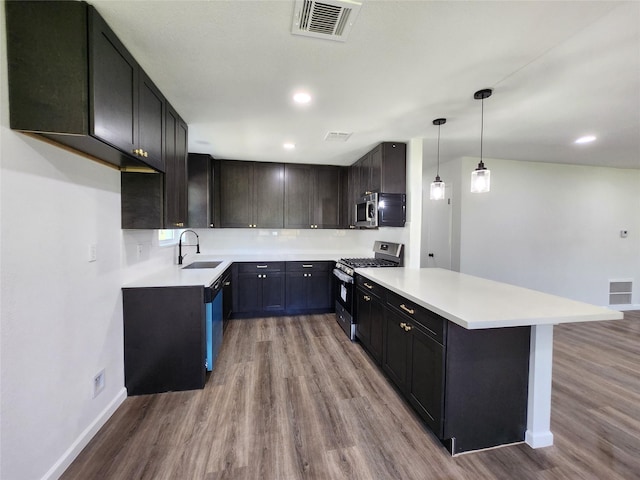 kitchen featuring wood finished floors, visible vents, a peninsula, a sink, and appliances with stainless steel finishes