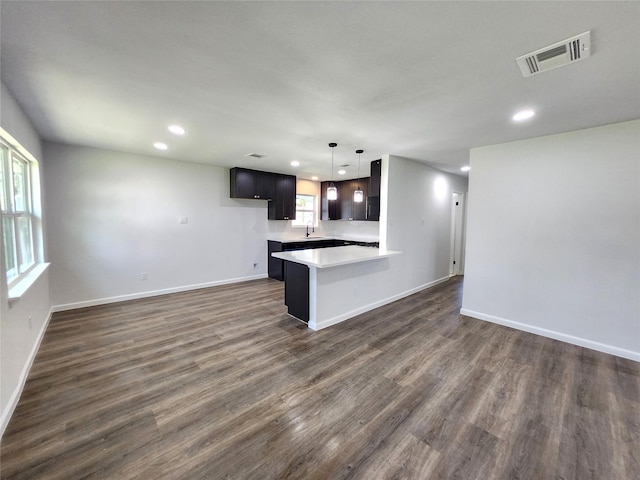 kitchen with visible vents, dark wood finished floors, a peninsula, a sink, and light countertops