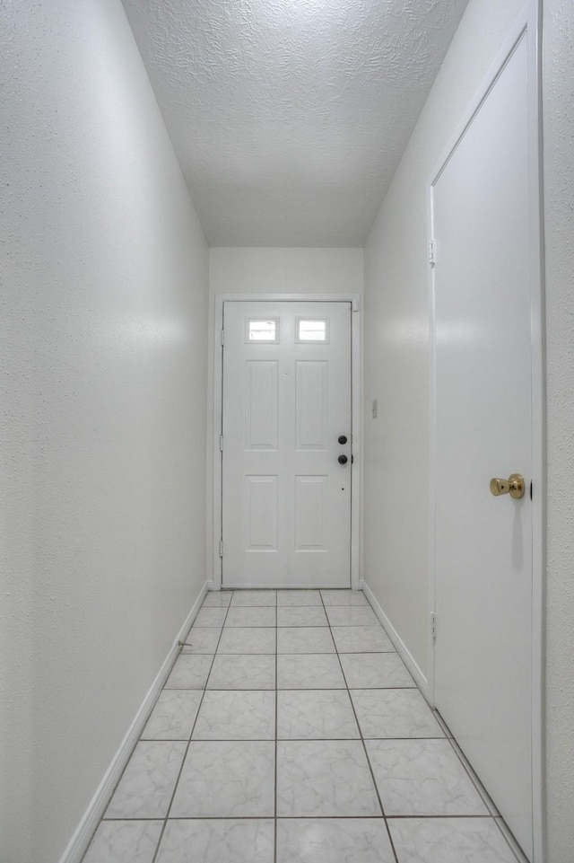 doorway to outside featuring light tile patterned flooring, a textured ceiling, and baseboards