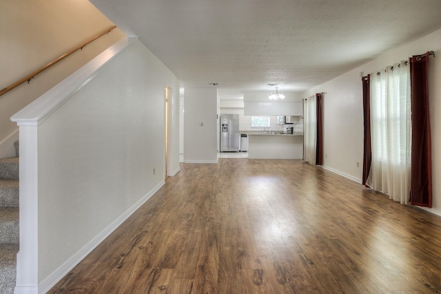 unfurnished living room with stairway, wood finished floors, baseboards, and a textured ceiling