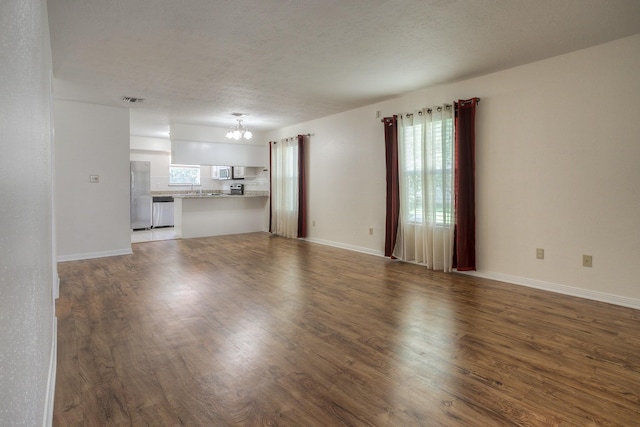 unfurnished living room featuring a notable chandelier, wood finished floors, and baseboards