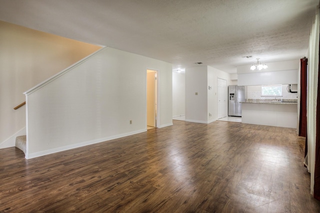 unfurnished living room featuring a notable chandelier, a textured ceiling, dark wood finished floors, baseboards, and stairs