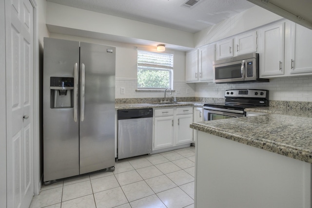 kitchen with a sink, backsplash, white cabinetry, appliances with stainless steel finishes, and light tile patterned floors