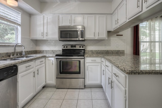 kitchen with a sink, backsplash, stainless steel appliances, white cabinets, and light tile patterned flooring