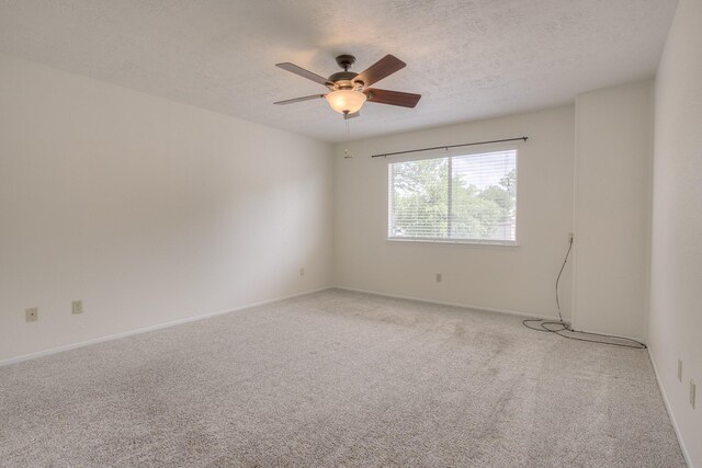 empty room with ceiling fan, light colored carpet, baseboards, and a textured ceiling