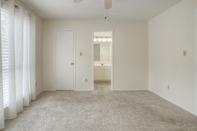 unfurnished bedroom featuring ensuite bath, multiple windows, light colored carpet, and baseboards