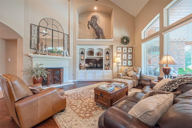 living area featuring built in features, wood finished floors, a towering ceiling, and a fireplace with raised hearth