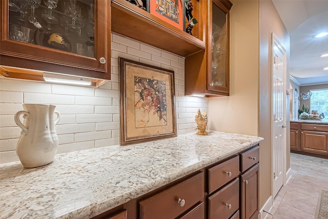 kitchen featuring light tile patterned floors, tasteful backsplash, glass insert cabinets, and light stone countertops