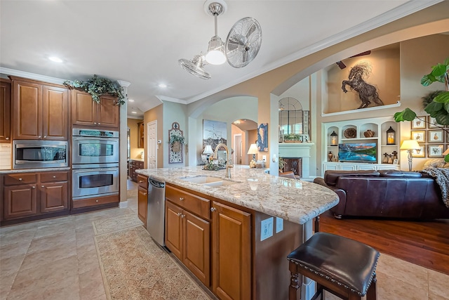 kitchen featuring a center island with sink, a sink, open floor plan, stainless steel appliances, and light stone countertops