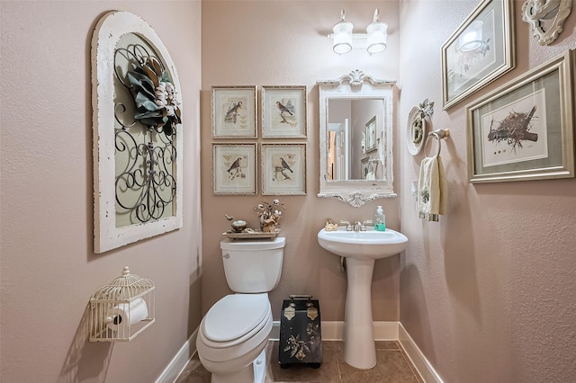 half bath featuring baseboards, toilet, and tile patterned flooring