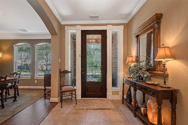 entryway with arched walkways, visible vents, crown molding, and baseboards