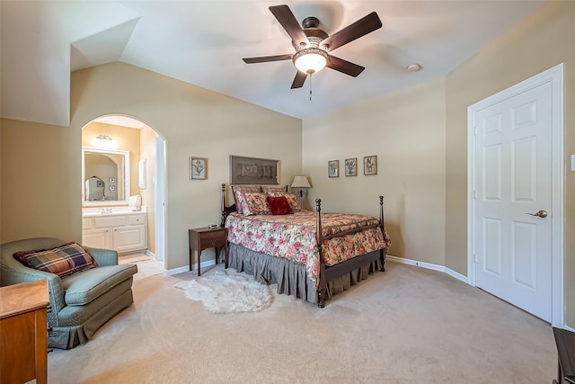 bedroom with light carpet, lofted ceiling, connected bathroom, arched walkways, and baseboards