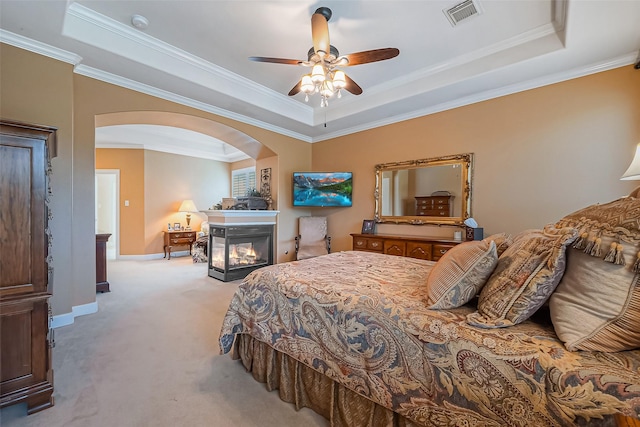 bedroom with a tray ceiling, visible vents, arched walkways, and light colored carpet