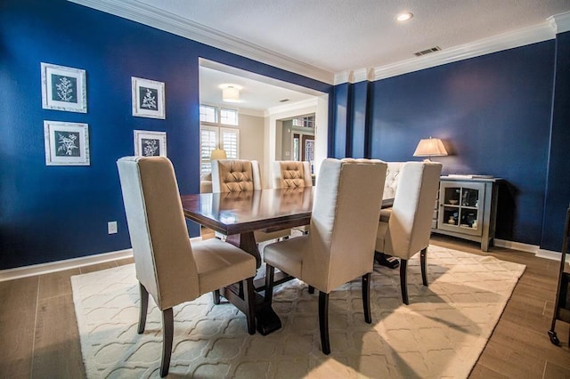 dining room featuring visible vents, wood finished floors, baseboards, and ornamental molding