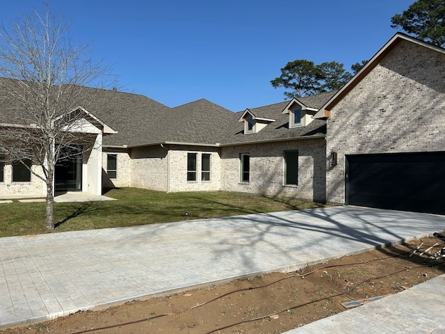 view of front of home with driveway, roof with shingles, a front yard, a garage, and brick siding