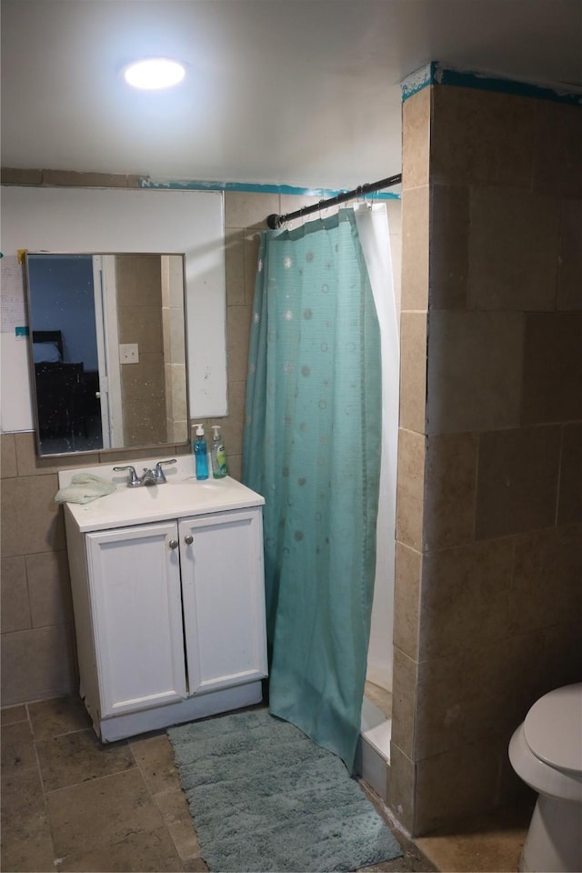 bathroom featuring tile walls, toilet, a shower with shower curtain, stone tile flooring, and vanity