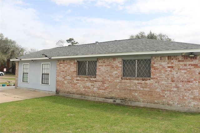 exterior space featuring brick siding, a lawn, and roof with shingles