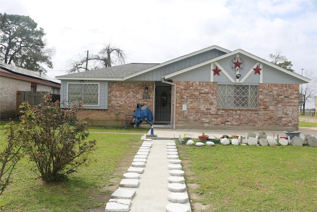 view of front of house featuring brick siding, roof with shingles, a front yard, and fence