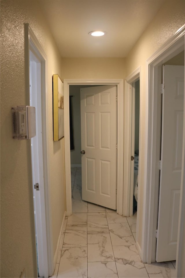 corridor with recessed lighting, marble finish floor, baseboards, and a textured wall