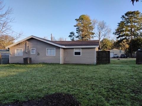 back of house with central AC unit, a lawn, and fence