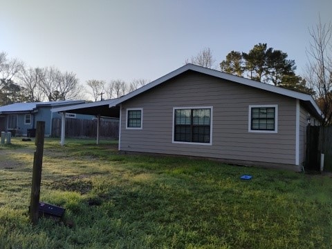 rear view of property with a carport, a lawn, and fence