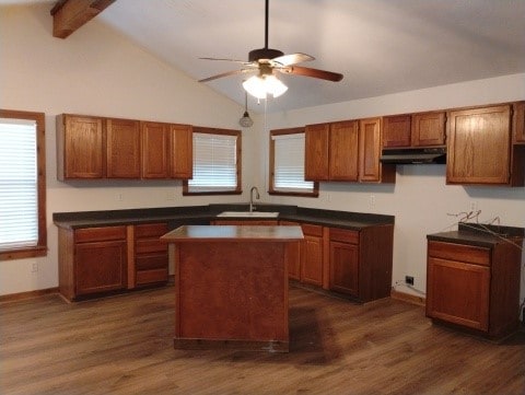 kitchen featuring lofted ceiling with beams, brown cabinets, under cabinet range hood, and a sink