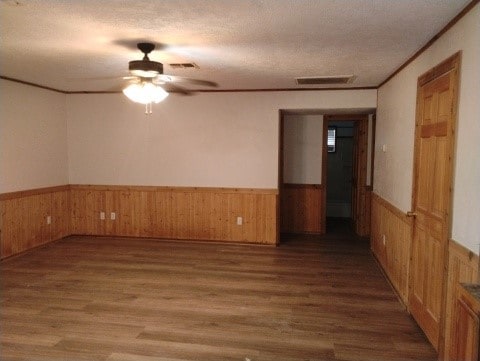 unfurnished room featuring a wainscoted wall, wood walls, a textured ceiling, and wood finished floors