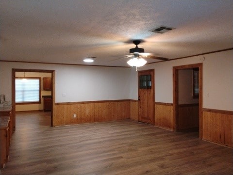 empty room with a textured ceiling, wood finished floors, visible vents, and wainscoting