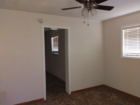 carpeted spare room featuring a ceiling fan and baseboards