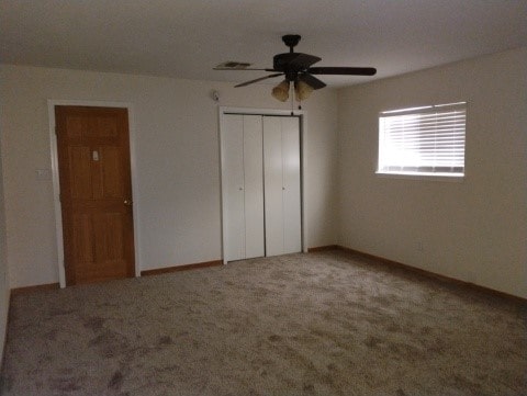 unfurnished bedroom with a closet, carpet floors, baseboards, and a ceiling fan