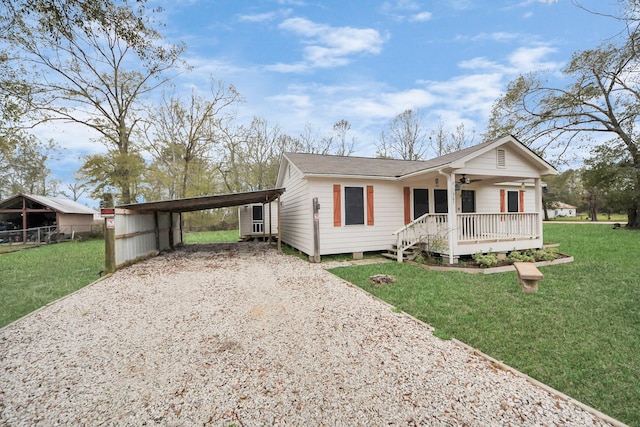 ranch-style home with a ceiling fan, gravel driveway, covered porch, a front yard, and a carport