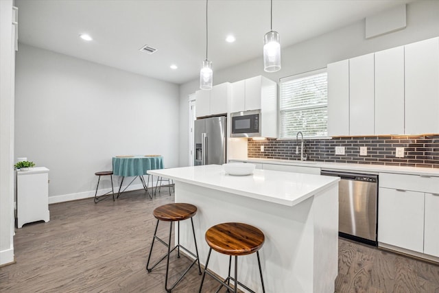 kitchen with visible vents, a kitchen bar, tasteful backsplash, wood finished floors, and appliances with stainless steel finishes