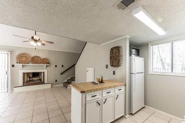 kitchen featuring a fireplace with raised hearth, freestanding refrigerator, light tile patterned flooring, white cabinetry, and a ceiling fan