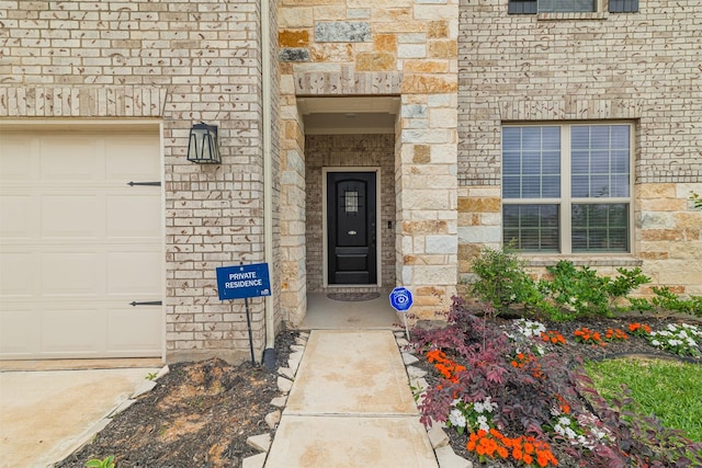 doorway to property with an attached garage, brick siding, and stone siding