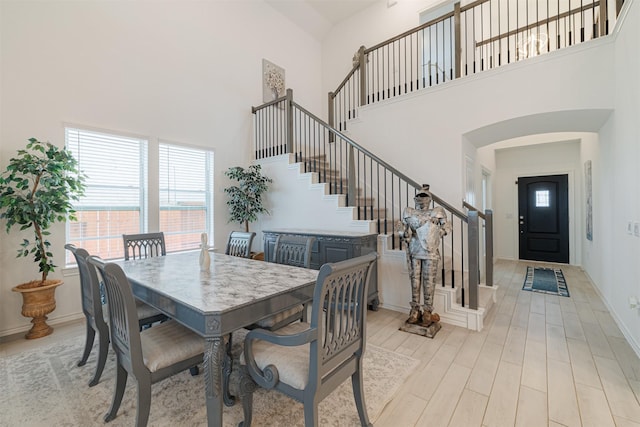 dining area with stairway, baseboards, wood finished floors, and a towering ceiling