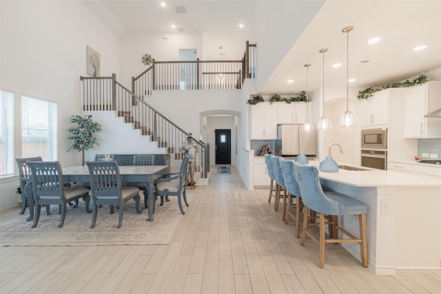 dining room featuring visible vents, arched walkways, a high ceiling, light wood finished floors, and stairs