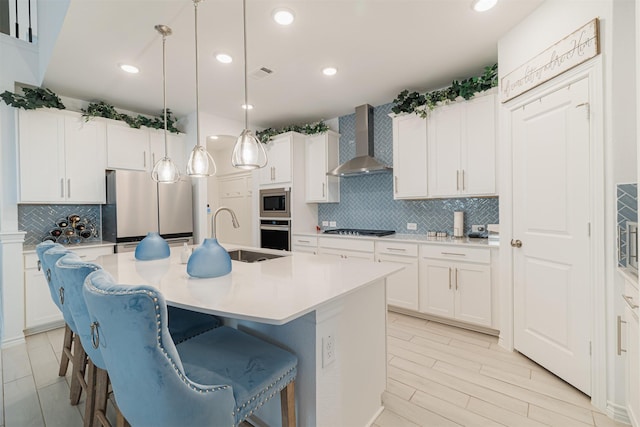 kitchen featuring visible vents, wall chimney range hood, a center island with sink, light countertops, and stainless steel appliances