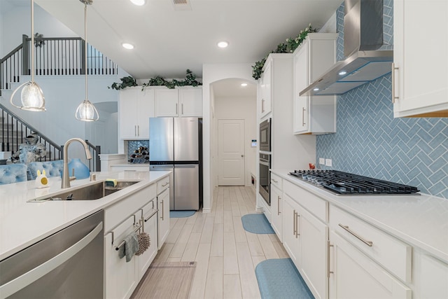 kitchen with a sink, wall chimney range hood, white cabinetry, appliances with stainless steel finishes, and light countertops