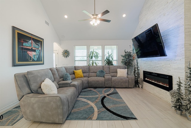 living area featuring wood finished floors, visible vents, high vaulted ceiling, ceiling fan, and a stone fireplace