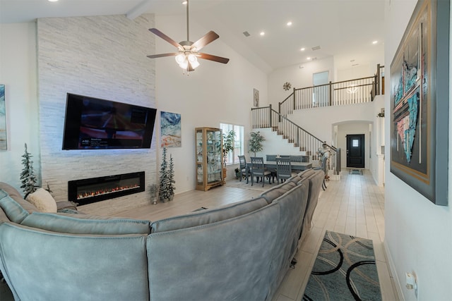 living area with beamed ceiling, stairs, a stone fireplace, wood finished floors, and high vaulted ceiling