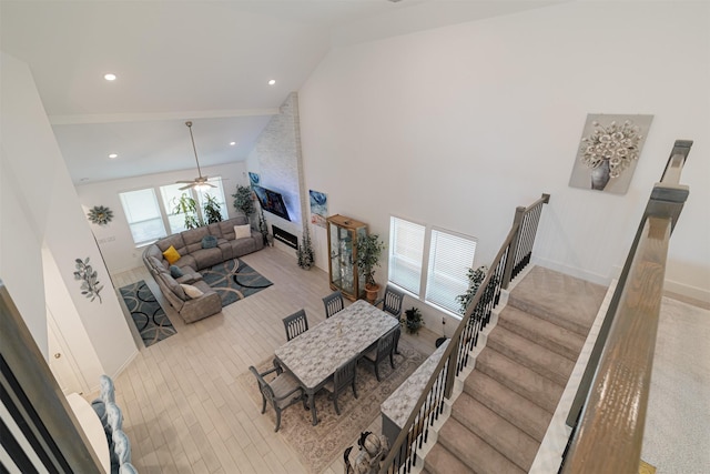 living area featuring ceiling fan, stairs, a fireplace, wood finished floors, and high vaulted ceiling