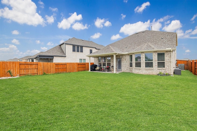 back of property featuring brick siding, a shingled roof, a lawn, a fenced backyard, and a patio