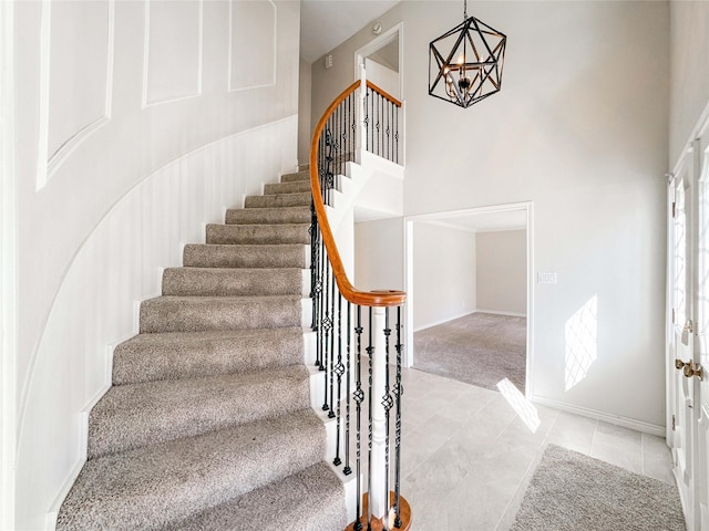 stairway featuring baseboards, carpet floors, a towering ceiling, tile patterned floors, and a chandelier