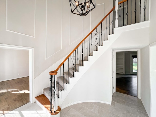 stairway with an inviting chandelier, baseboards, a towering ceiling, and wood finished floors