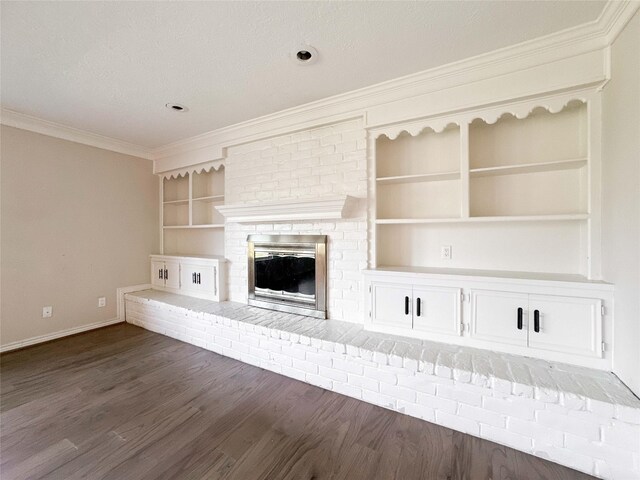 unfurnished living room with built in shelves, dark wood-type flooring, ornamental molding, baseboards, and a brick fireplace